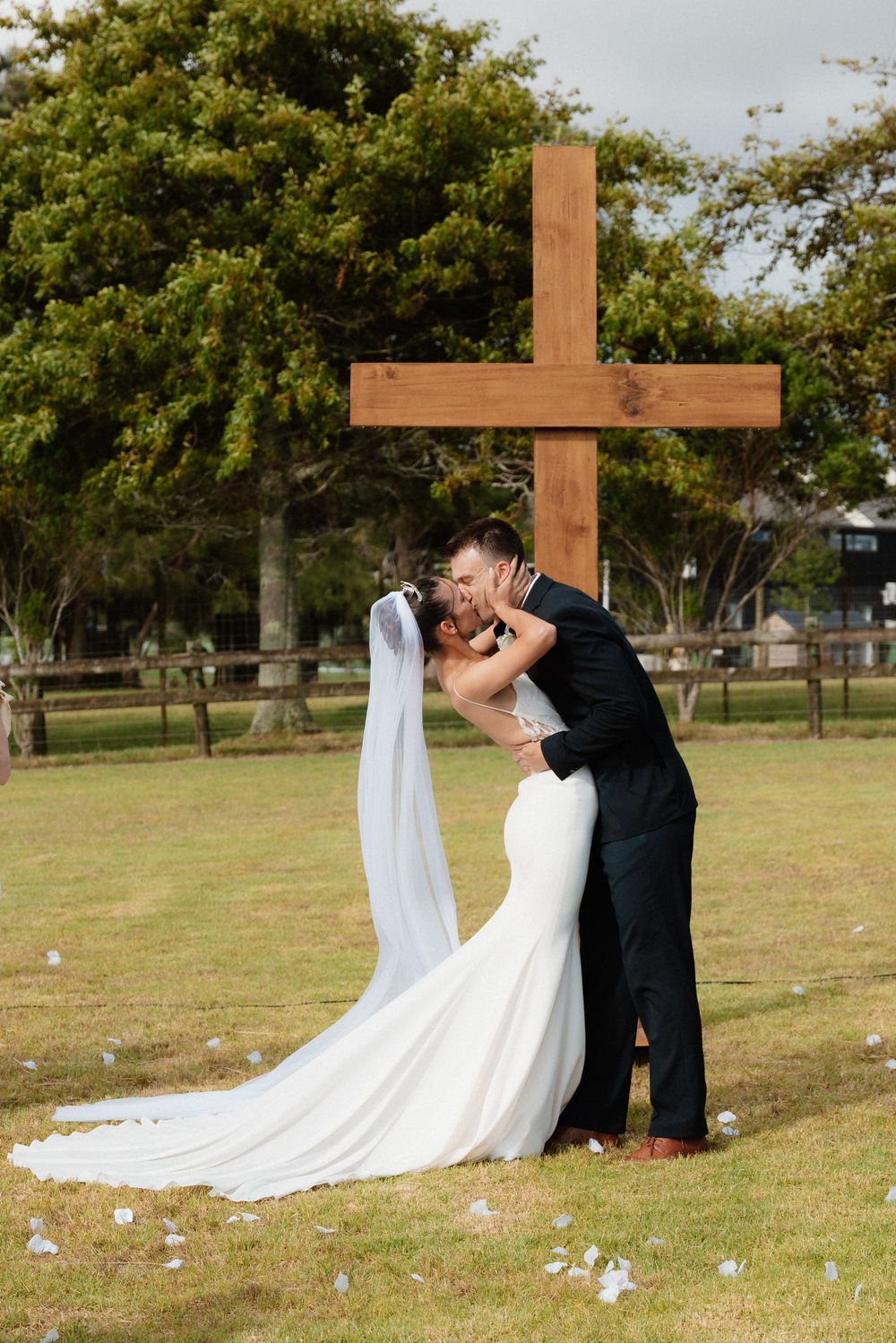 A couple shares a romantic moment during their outdoor wedding ceremony with a wooden cross in the background.