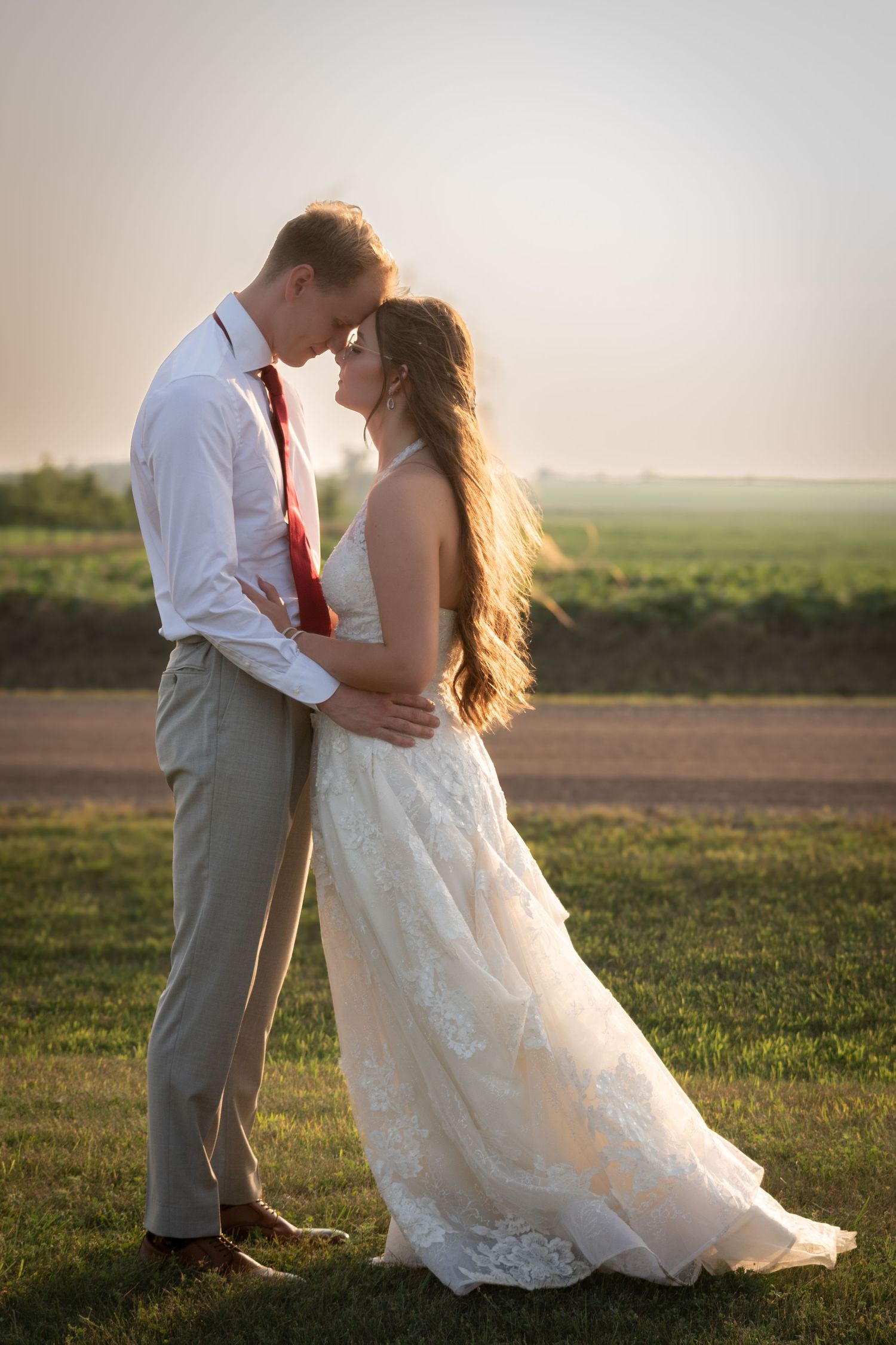 A bride and groom leaning in for a kiss with a sunset and field in the background.
