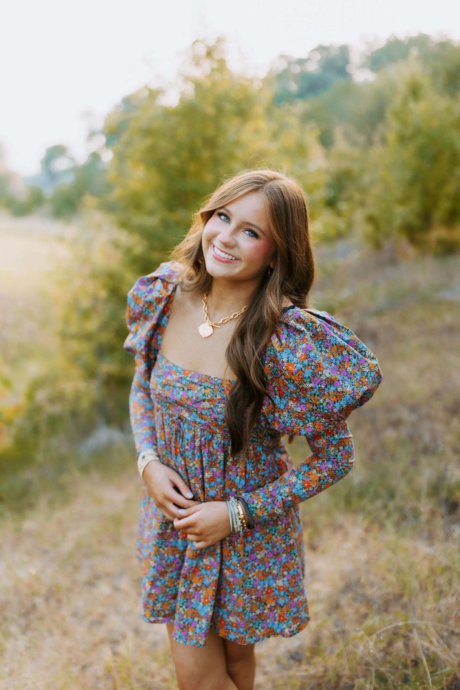 A person poses outdoors in a floral print dress with puff sleeves against a natural autumn background.