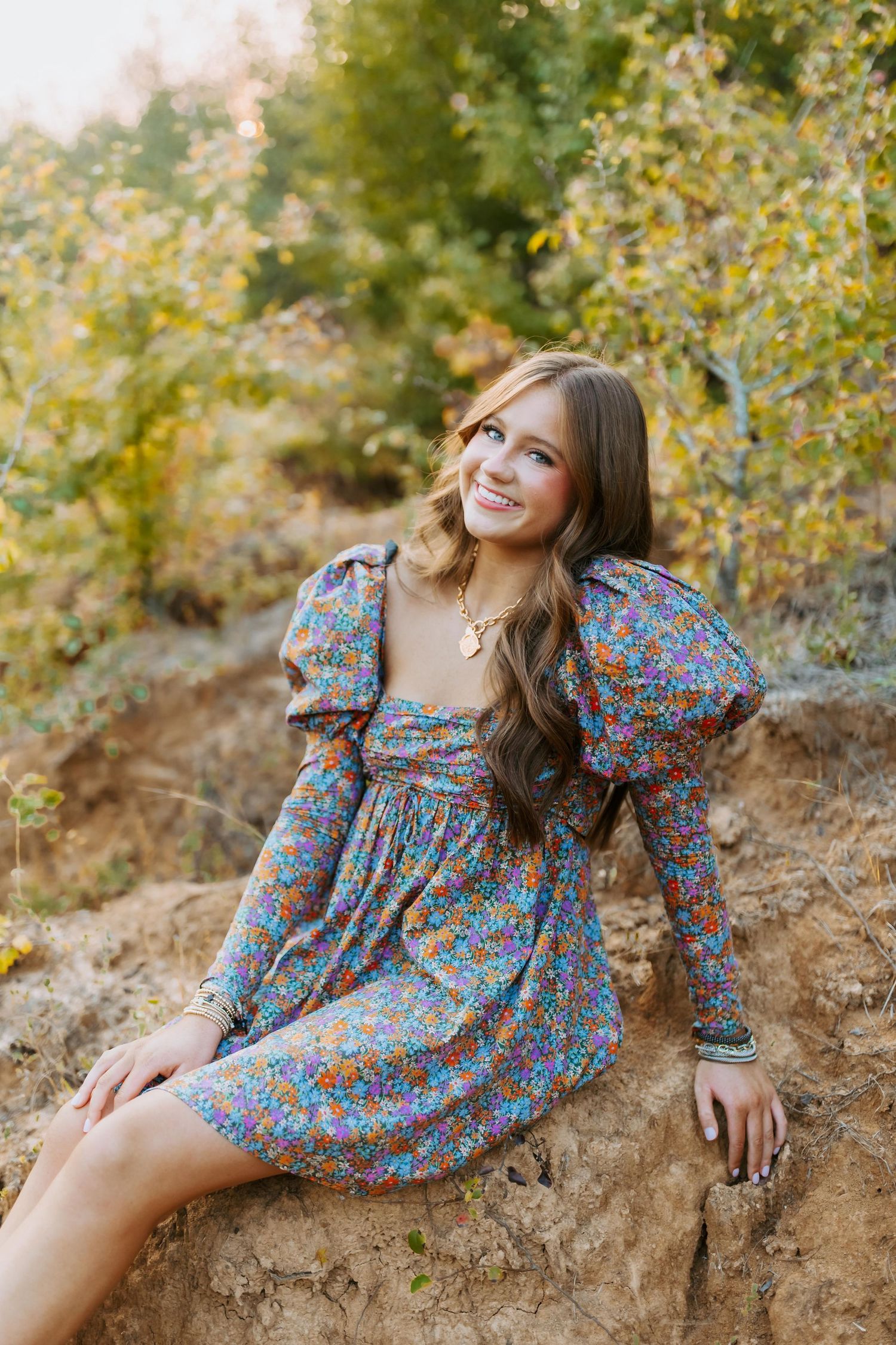 A floral print prairie dress with puff sleeves is worn while sitting on a rocky hillside during golden hour.