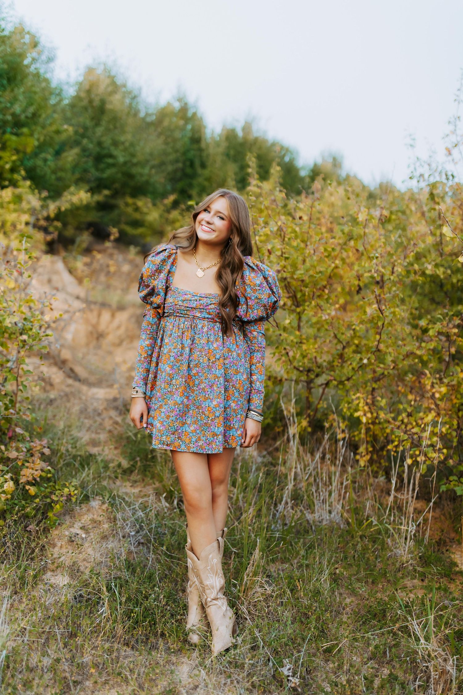 A feminine fall fashion look featuring a floral dress with statement sleeves and tall boots in an outdoor setting.