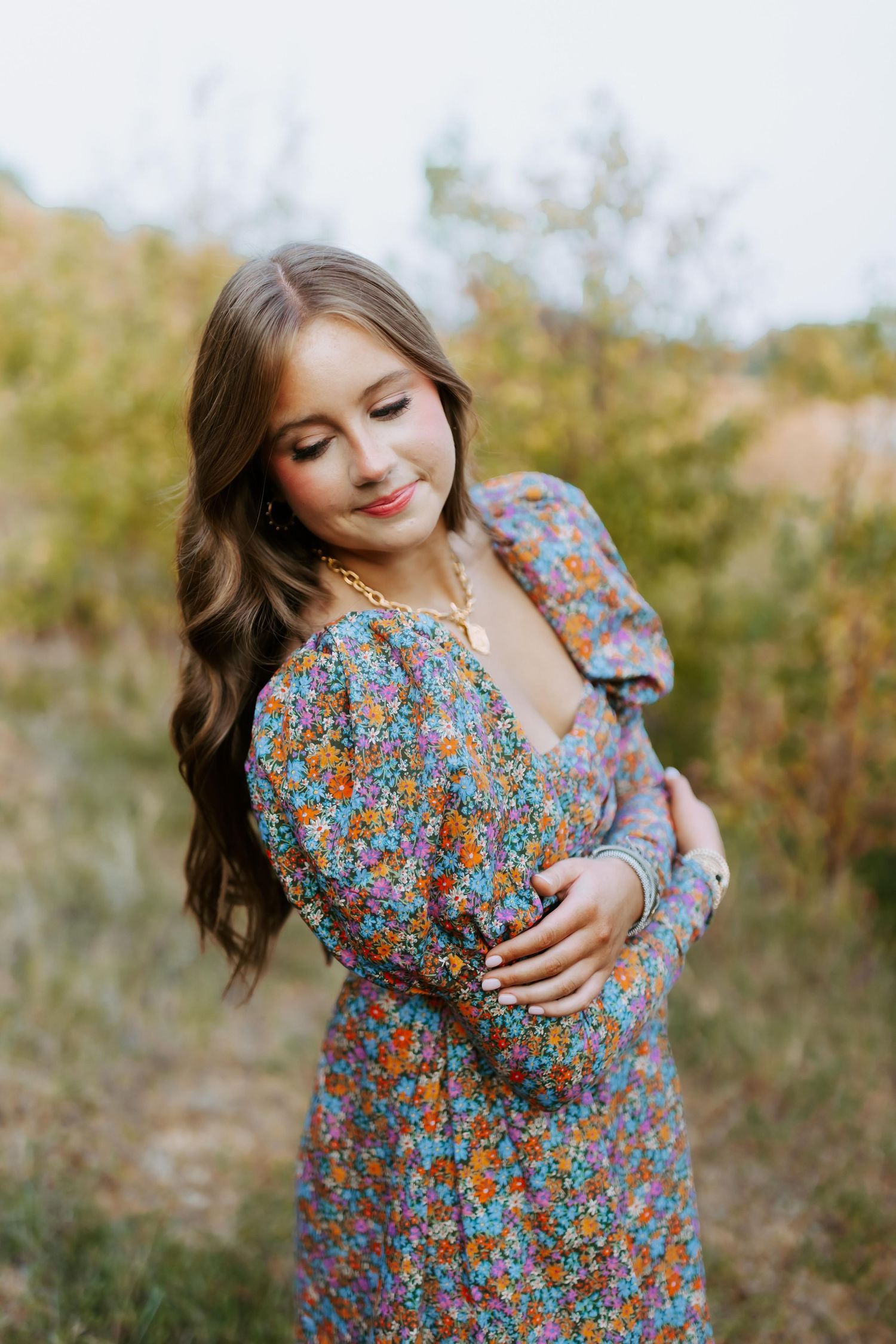Person in floral print dress with puff sleeves poses outdoors in natural setting during golden hour.