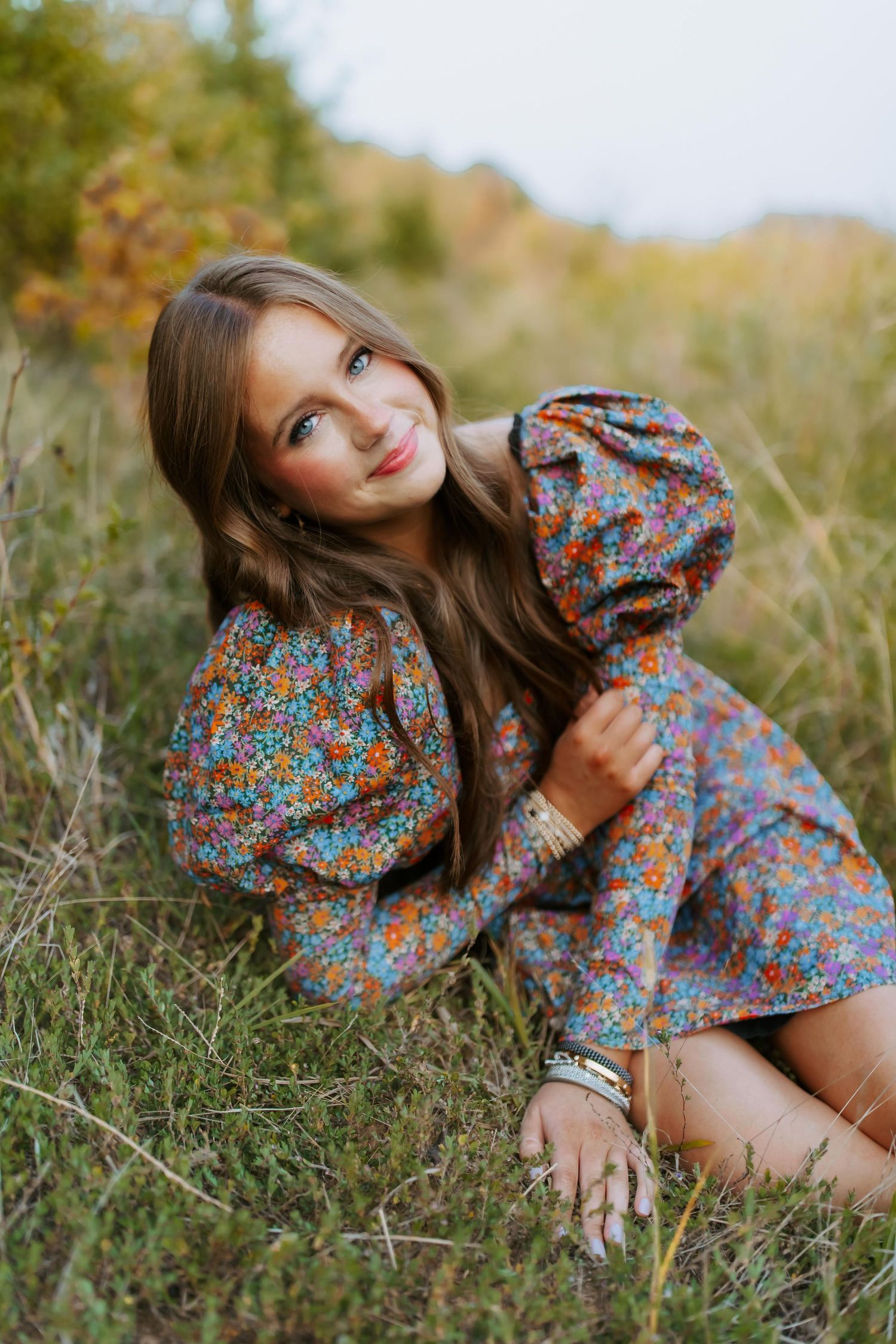 A person in a floral print dress sits in a grassy field during autumn.