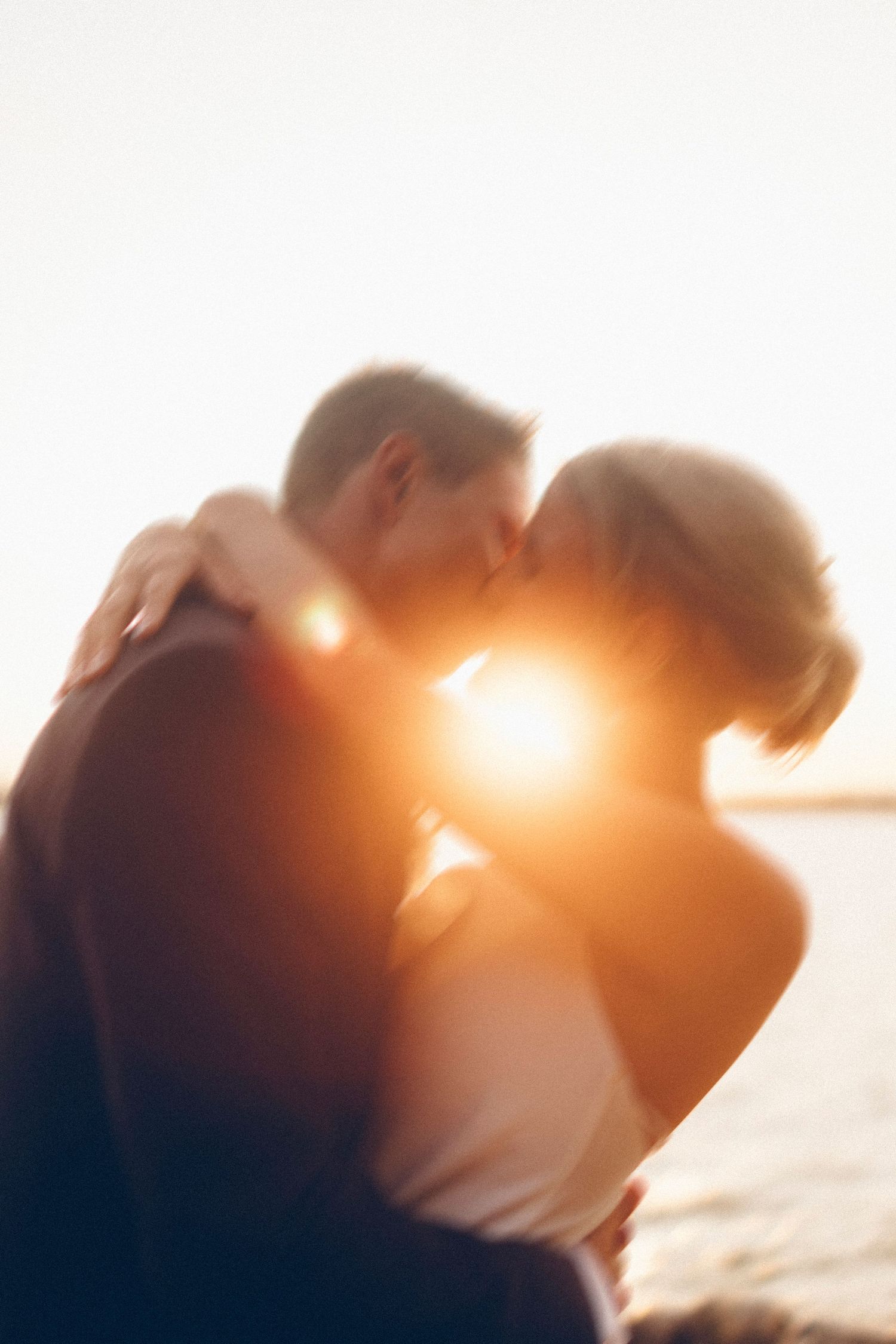 Silhouetted couple sharing intimate moment with sun flare.