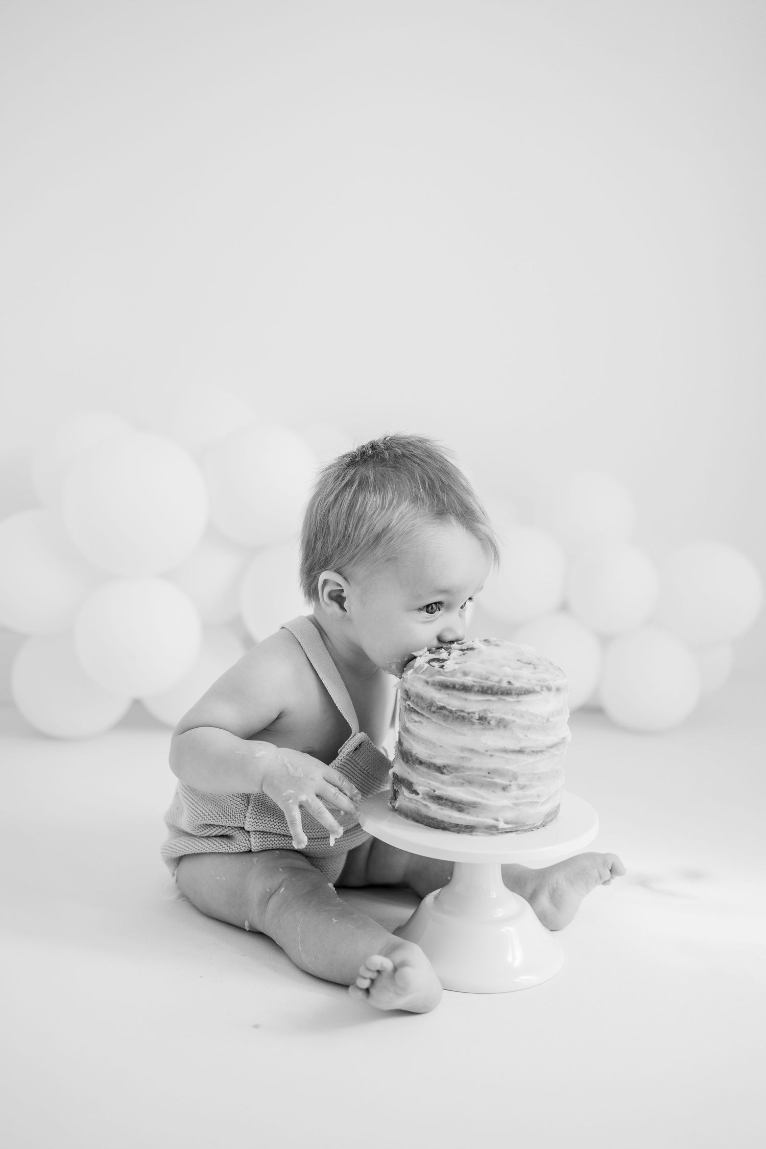 Small baby splashing in white bathtub with yellow and sage green balloon arch backdrop for photo session.