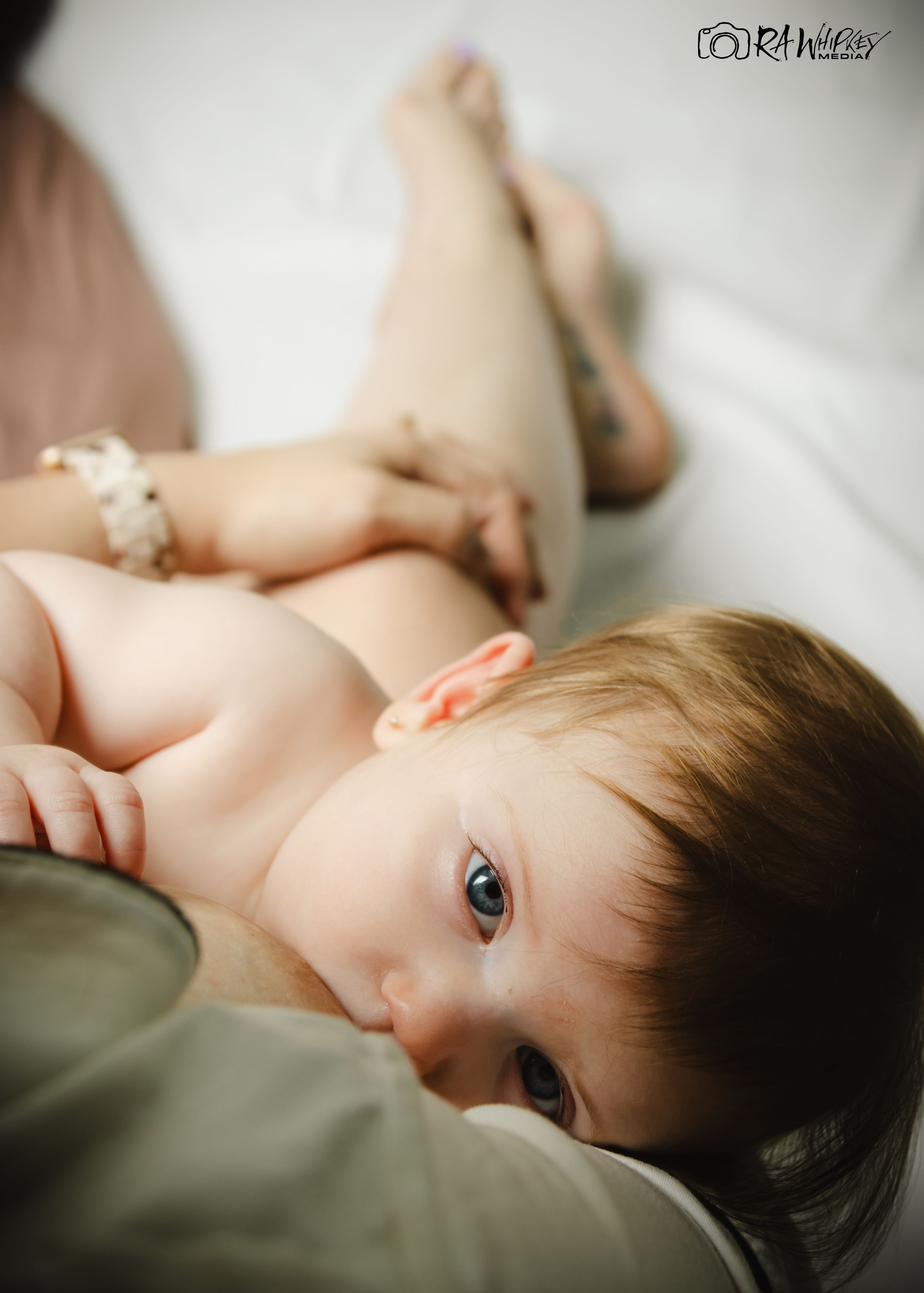 Baby with dark hair lying on side against muted fabric background.