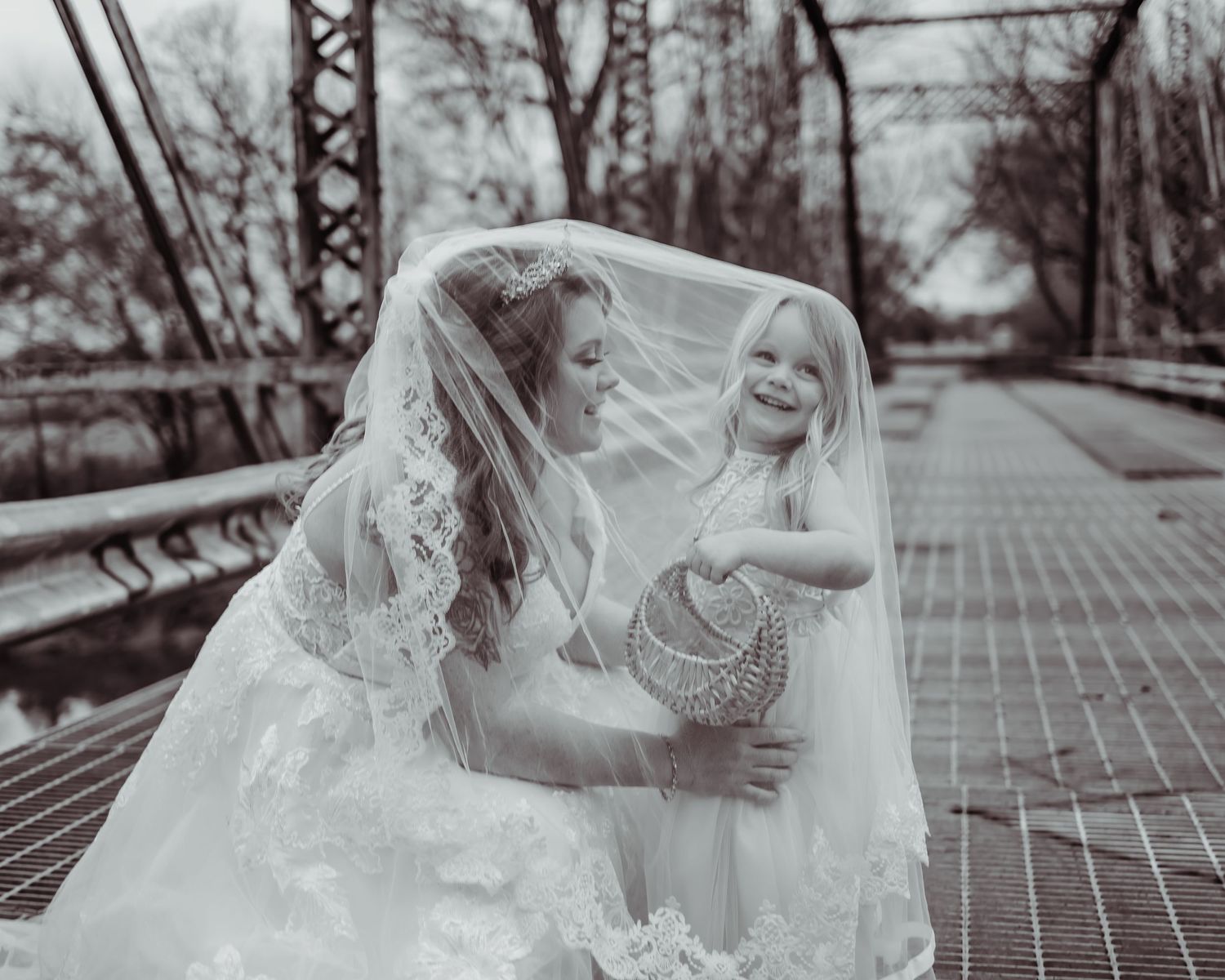A tender black and white moment shared under a flowing bridal veil on a brick path surrounded by winter trees.
