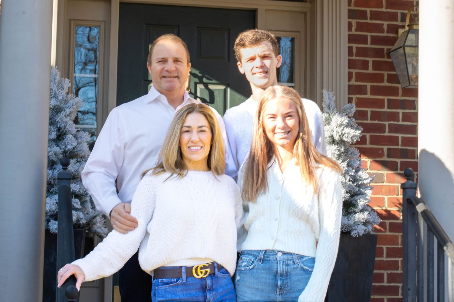 A family stands together on their front porch with white winter decorations.