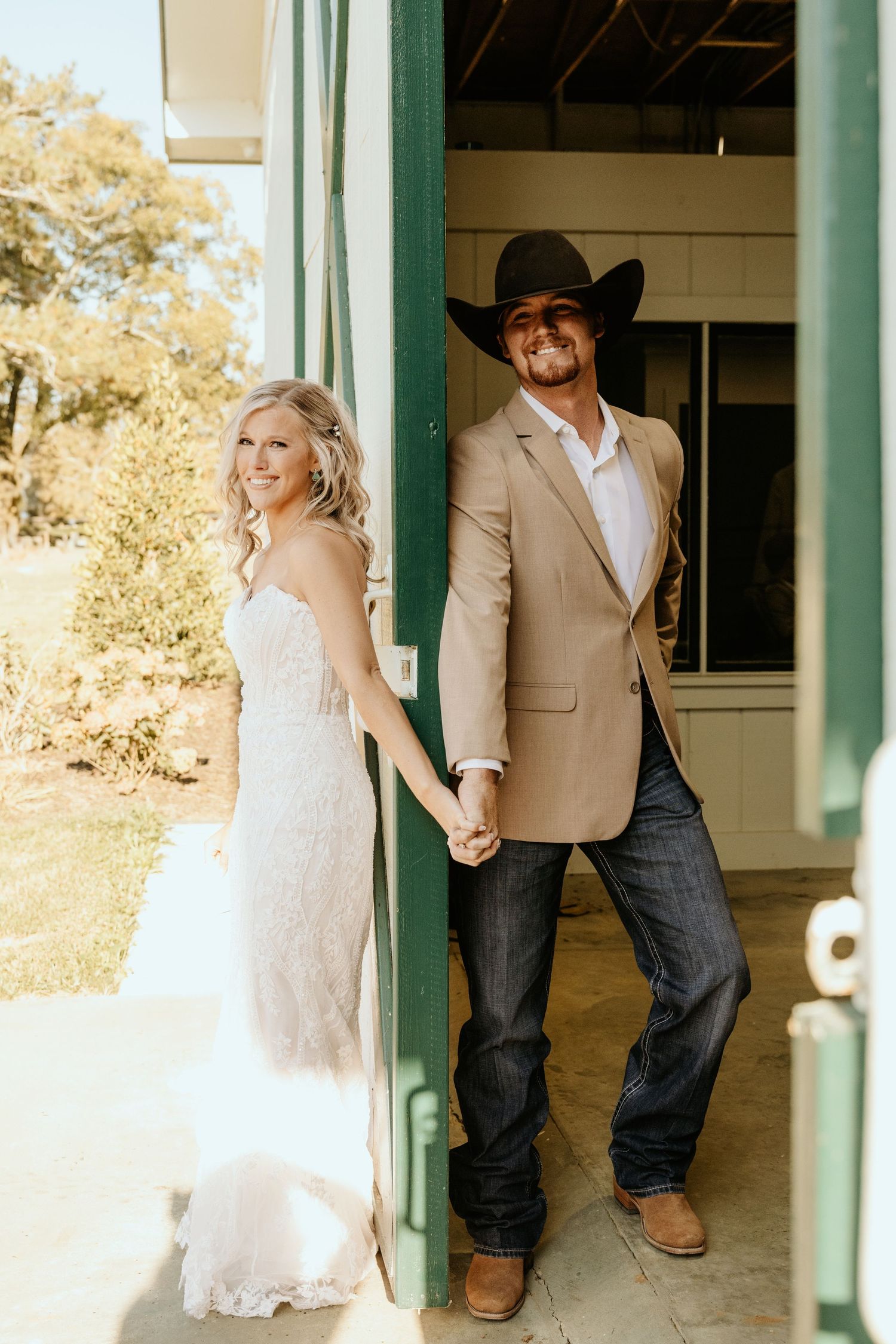 Couple in western wedding attire posing in doorway of rustic green-trimmed building.