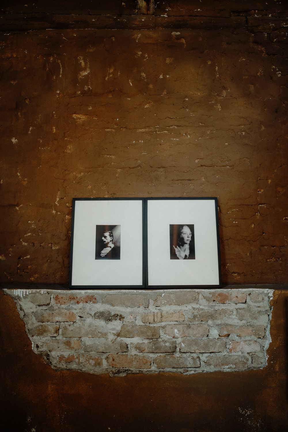 Two framed black and white photographs mounted on exposed brick wall with dark background.