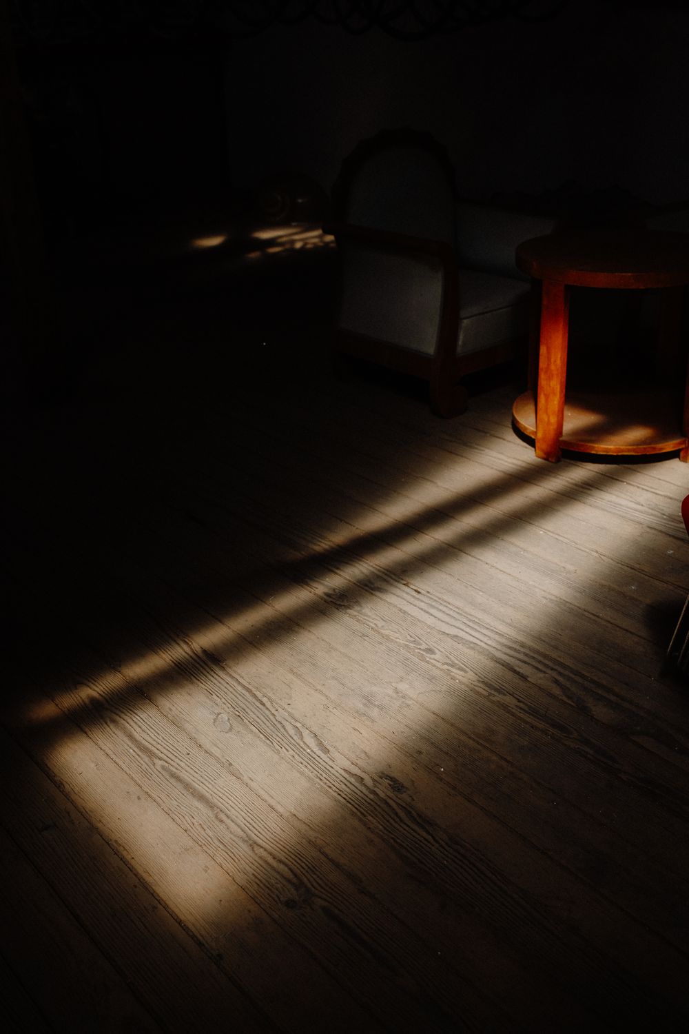 Dramatic shadows cast across wooden floorboards in dark room with warm lighting.