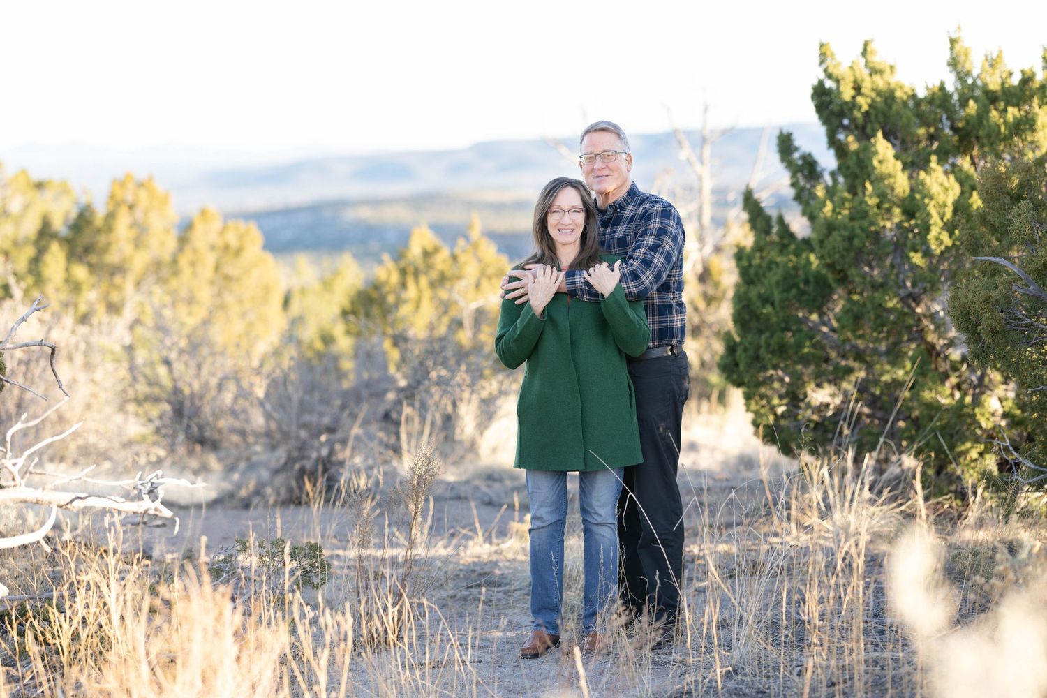 Affectionate couple stands close together on nature path with mountains in background.