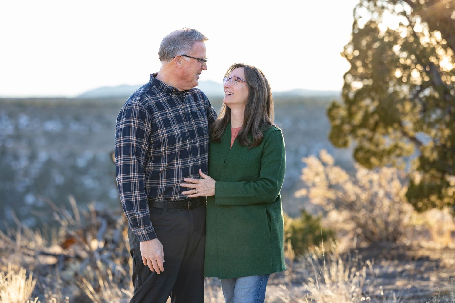 Stylish couple shares tender moment while standing on desert trail with mountain backdrop.