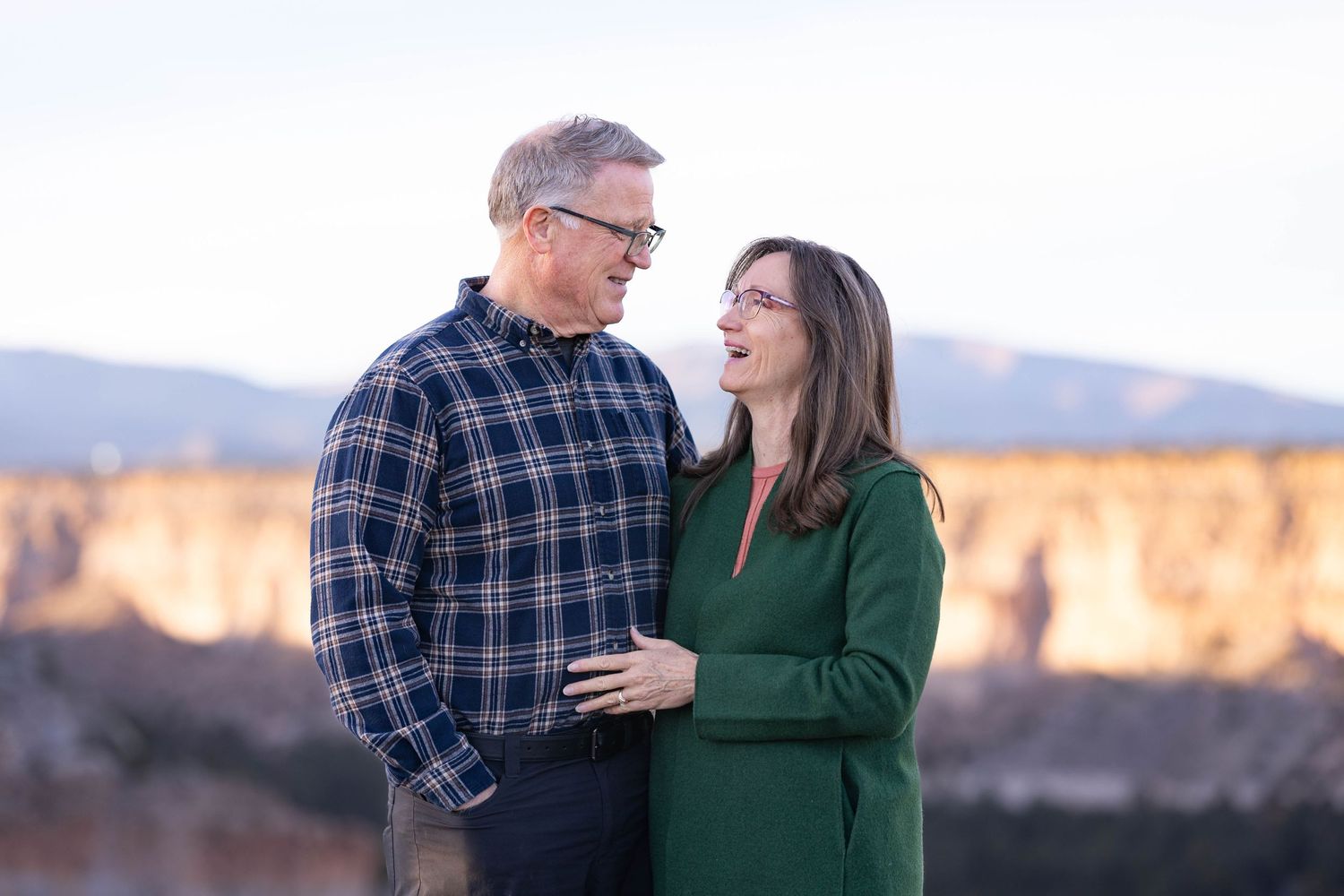 Couple shares romantic moment against backdrop of desert cliffs during golden hour.