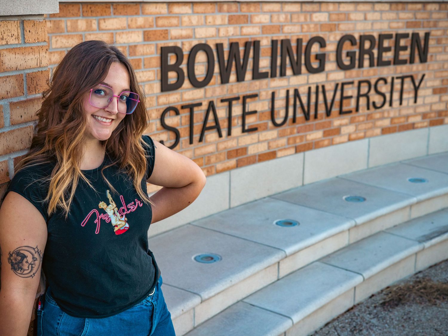 Student poses in front of Bowling Green State University brick sign wearing casual attire.