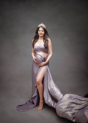 An elegant maternity photo in flowing lilac gown with side slit against dark background.
