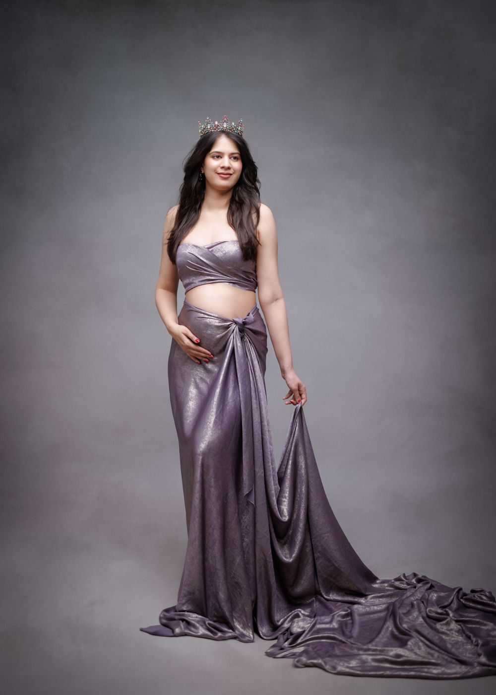 A sophisticated maternity portrait in two-piece lavender silk gown against grey backdrop.