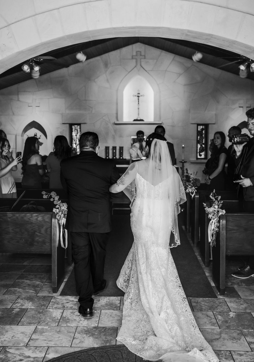 Black and white photo of wedding ceremony in traditional church with bride in flowing dress.