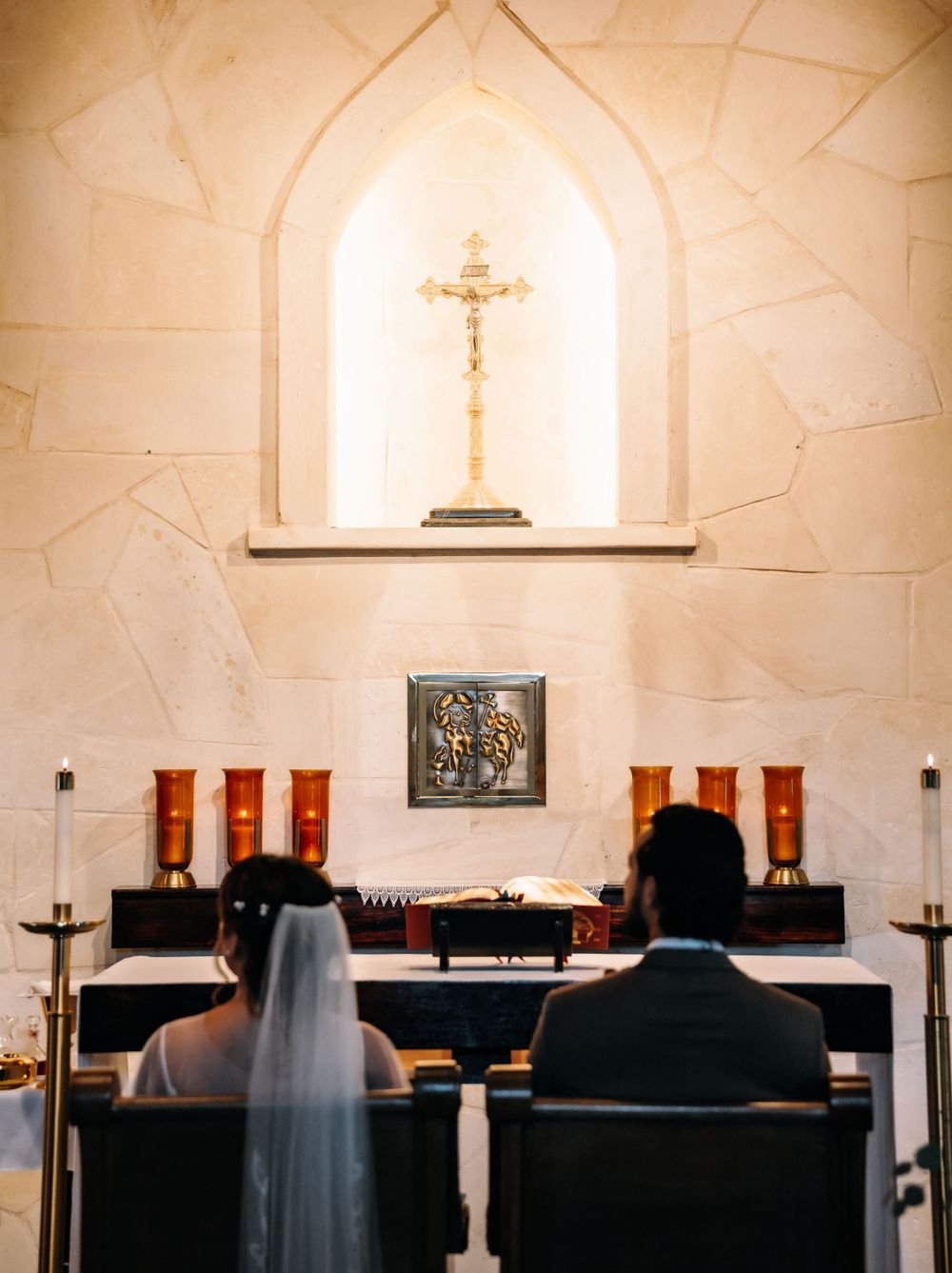 View of church altar with crucifix and couple seated during wedding ceremony.