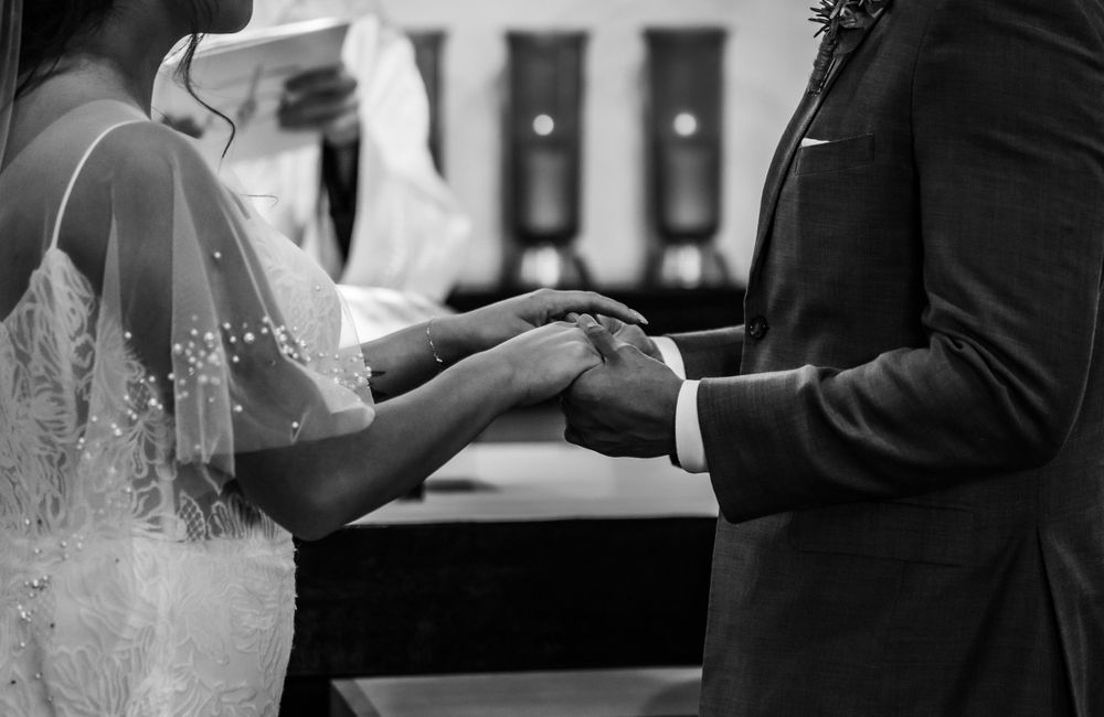 Black and white close-up of couple holding hands during wedding ceremony.