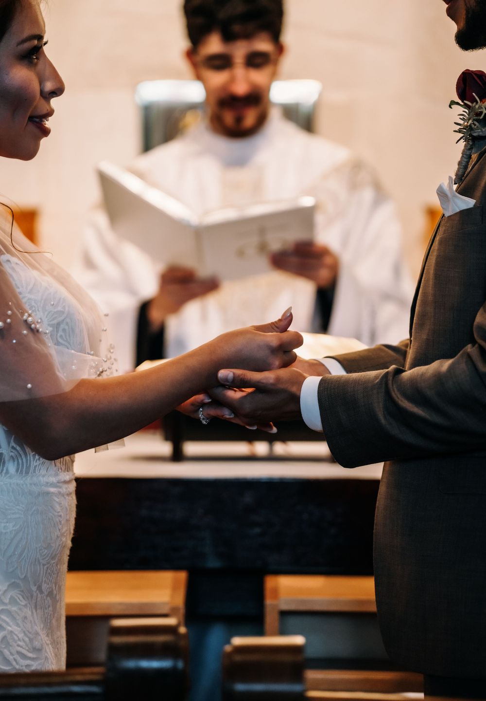 Couple exchanging rings during wedding ceremony with officiant in background.