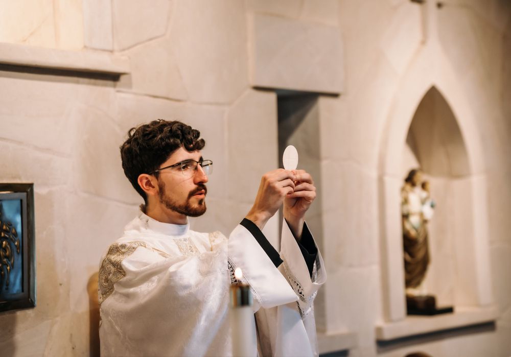 A robed clergy member holds up a lit candle during a religious service in a church.