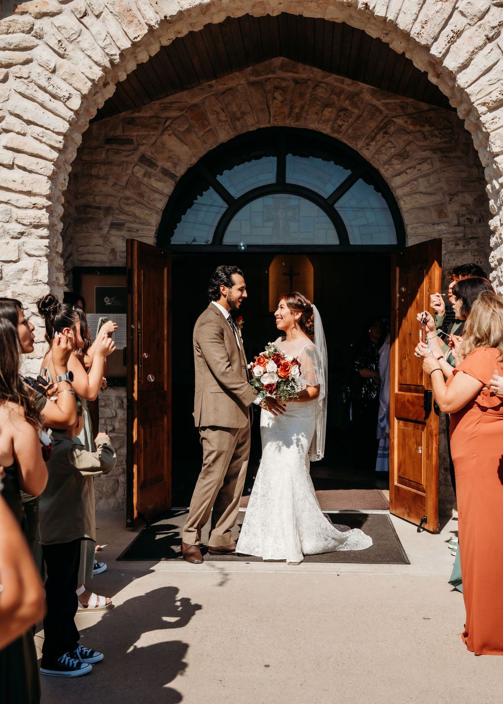 A wedding ceremony takes place under a stone archway entrance with guests in formal attire.