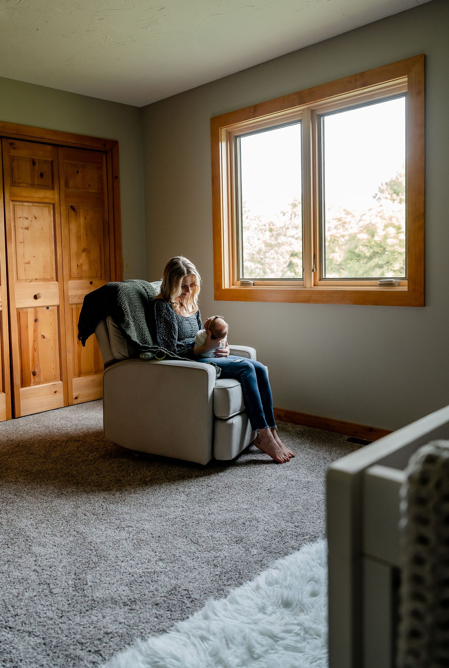 Person sitting alone in armchair by window in sparsely furnished room with wooden trim.