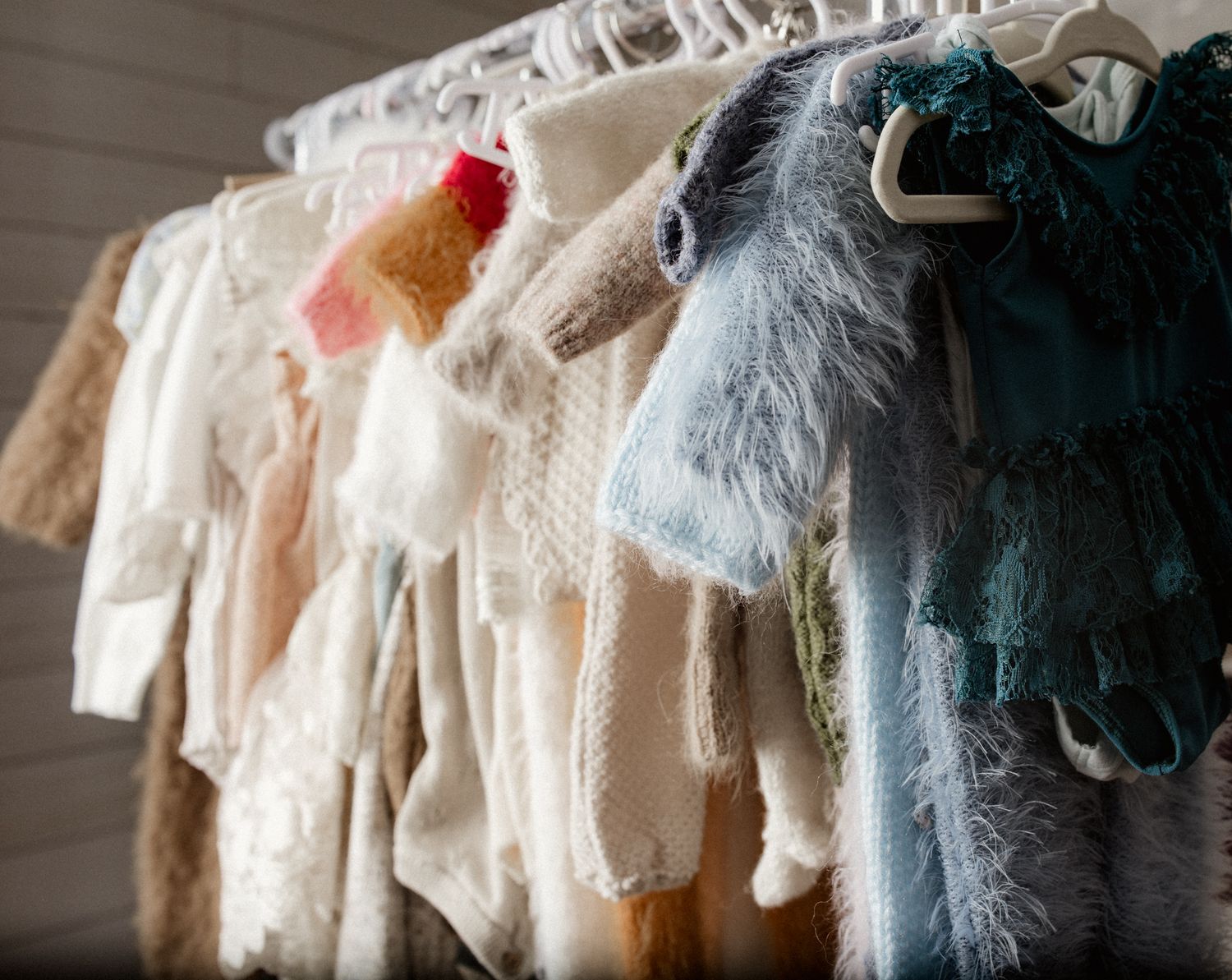 Close-up of newborn and baby photography studio wardrobe rack with cream and teal fluffy outfits.