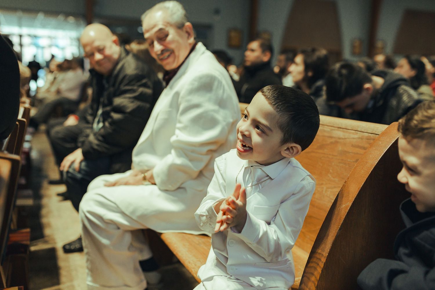 Child smiling as he sits in church with older men around him smiling at his joy