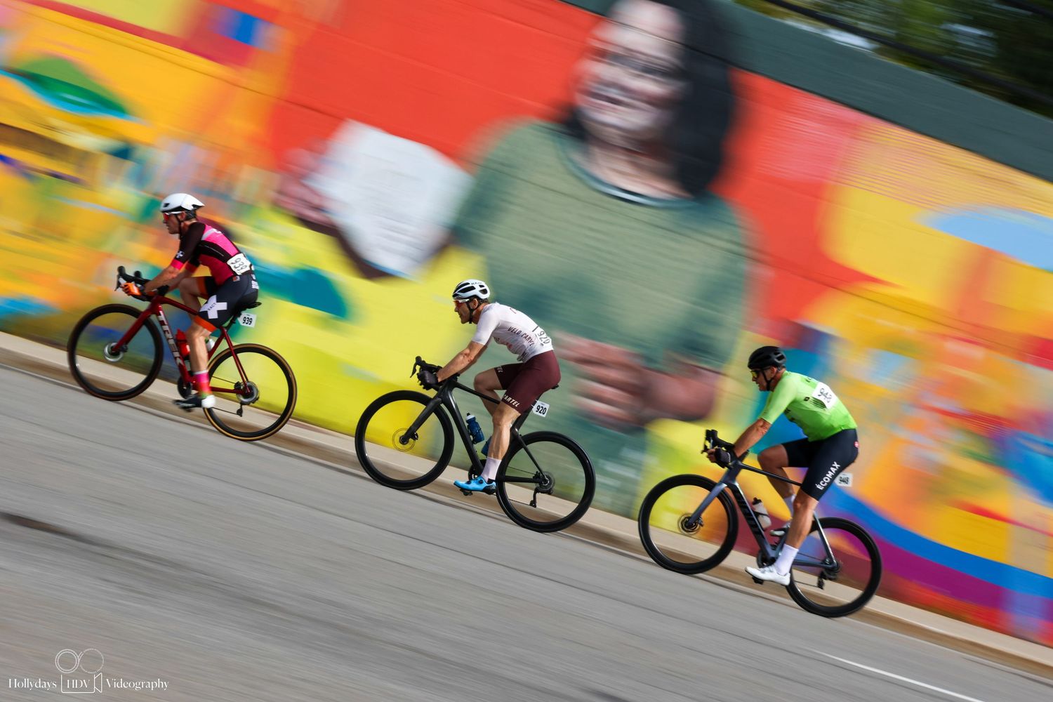 Three cyclists racing past a colorful blurred wall background during a cycling competition.