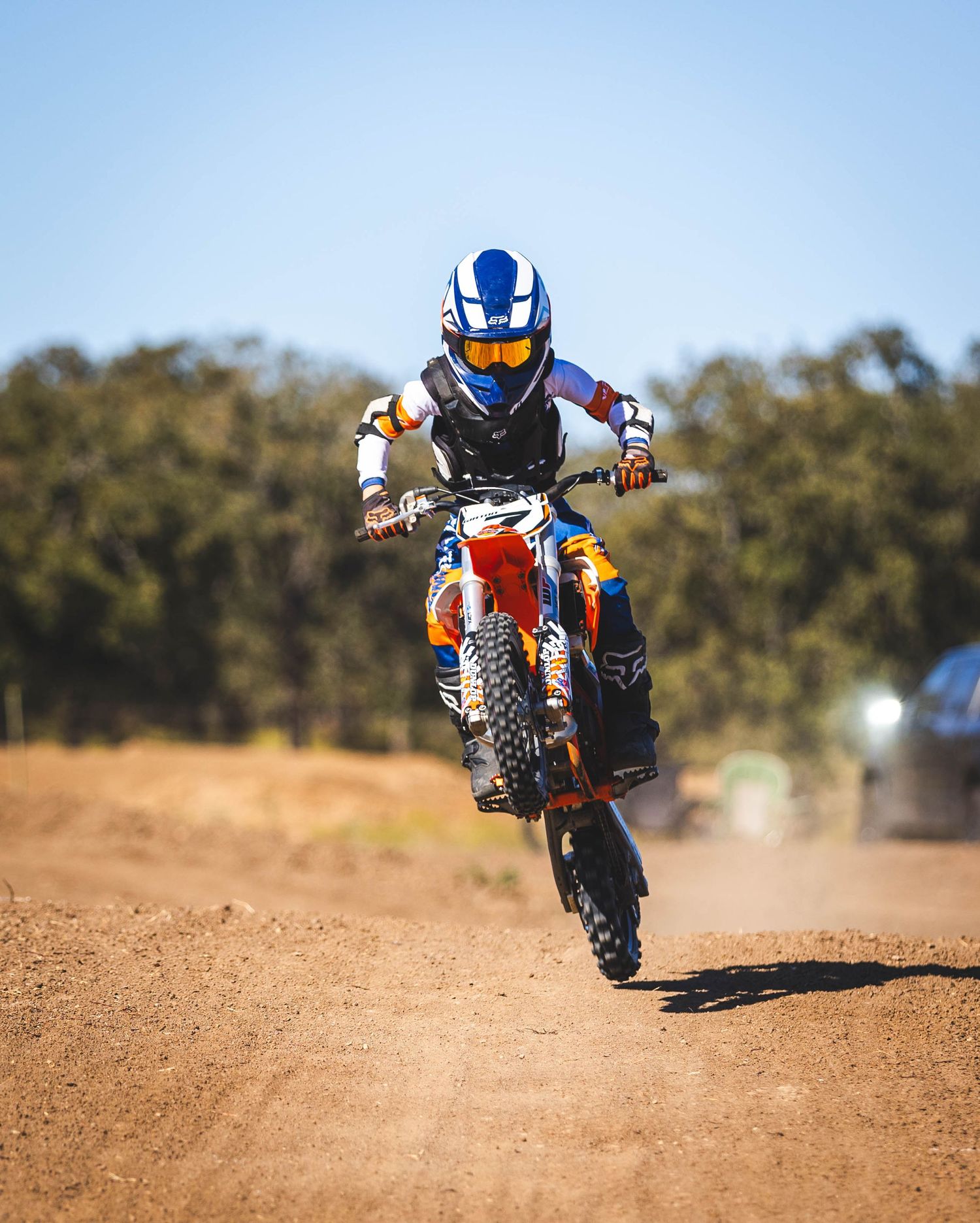 Motocross rider in blue helmet performing wheelie on dirt track.