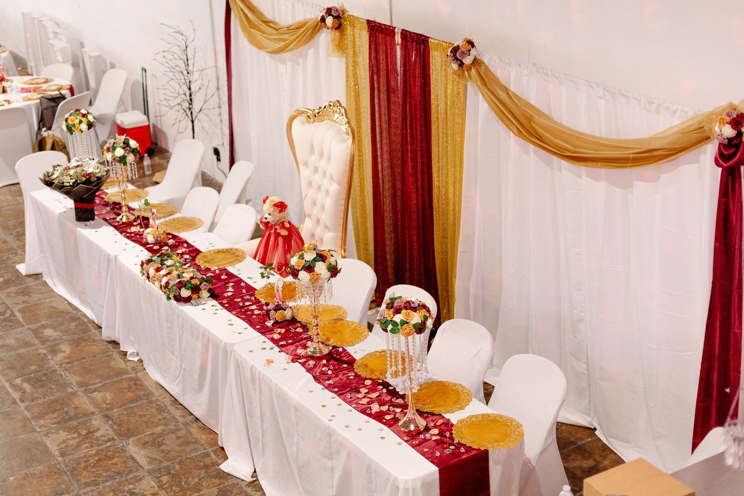 Elegant quinceanera head table decorated with red and gold draping and floral arrangements.