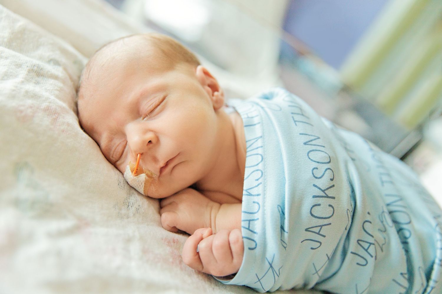 Peaceful sleeping newborn baby swaddled in light blue blanket rests on soft white hospital bedding.