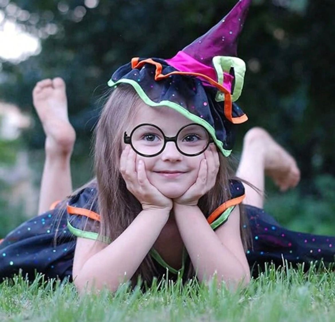 A person lying on grass wearing a colorful hat and glasses.