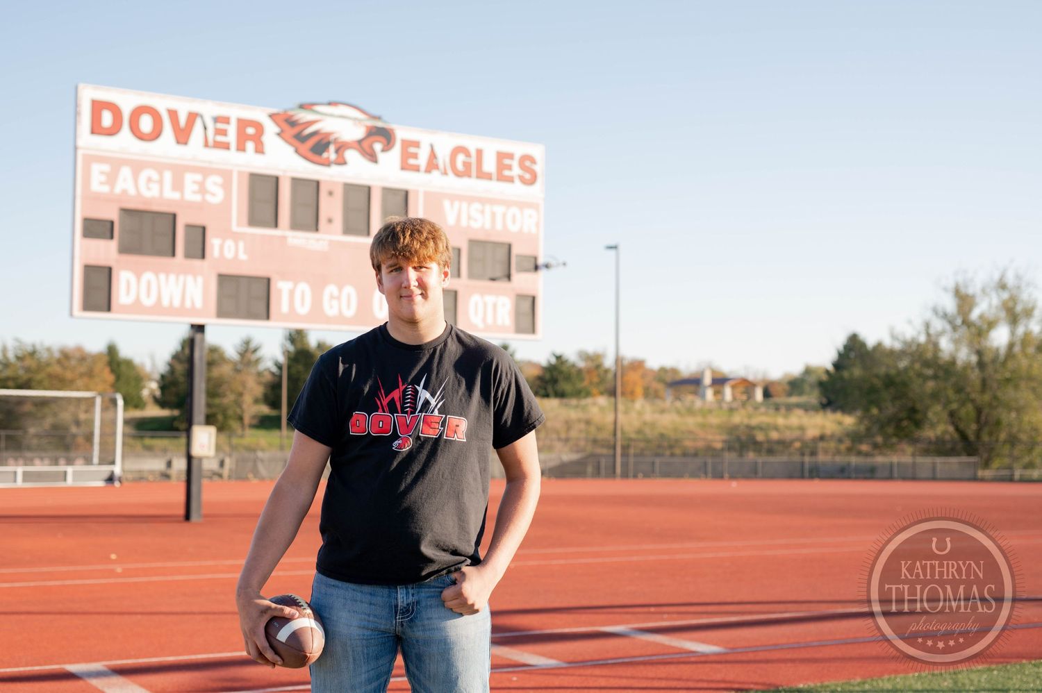 Football player poses with ball in front of Dover Eagles scoreboard on athletic field.