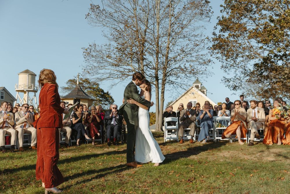 People gather on a grassy hillside for an outdoor autumn event with houses visible in the background.