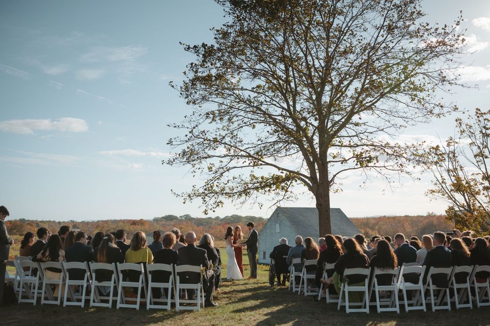 A panoramic view of white chairs set up for an outdoor wedding ceremony against a scenic mountain backdrop at sunset.