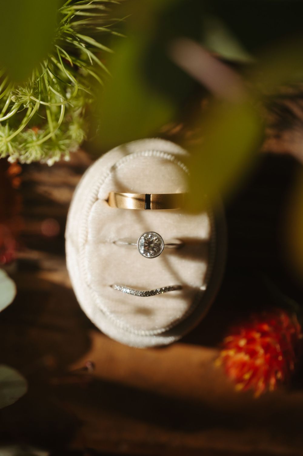 A white engagement ring on a dark wooden surface with a blurred orange flower in the background.