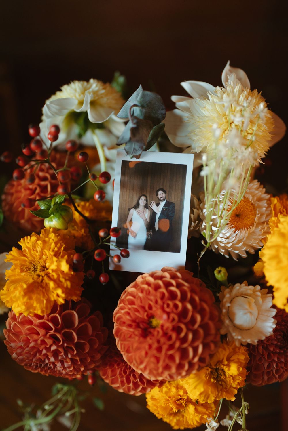 Orange and yellow flowers arranged with polaroid photos in a rustic wedding centerpiece.