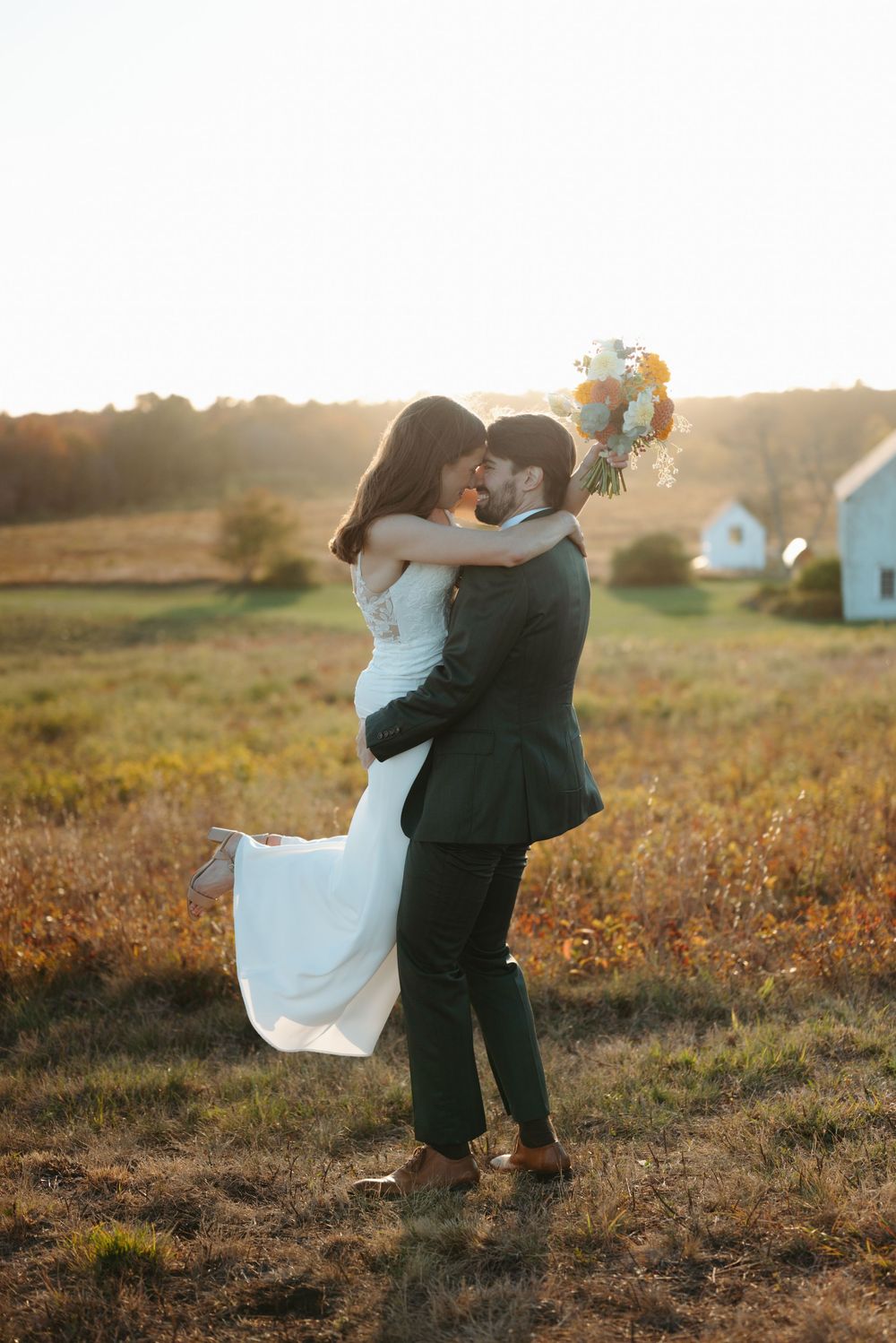 A couple in formal attire dances together in a golden sunlit field at sunset.