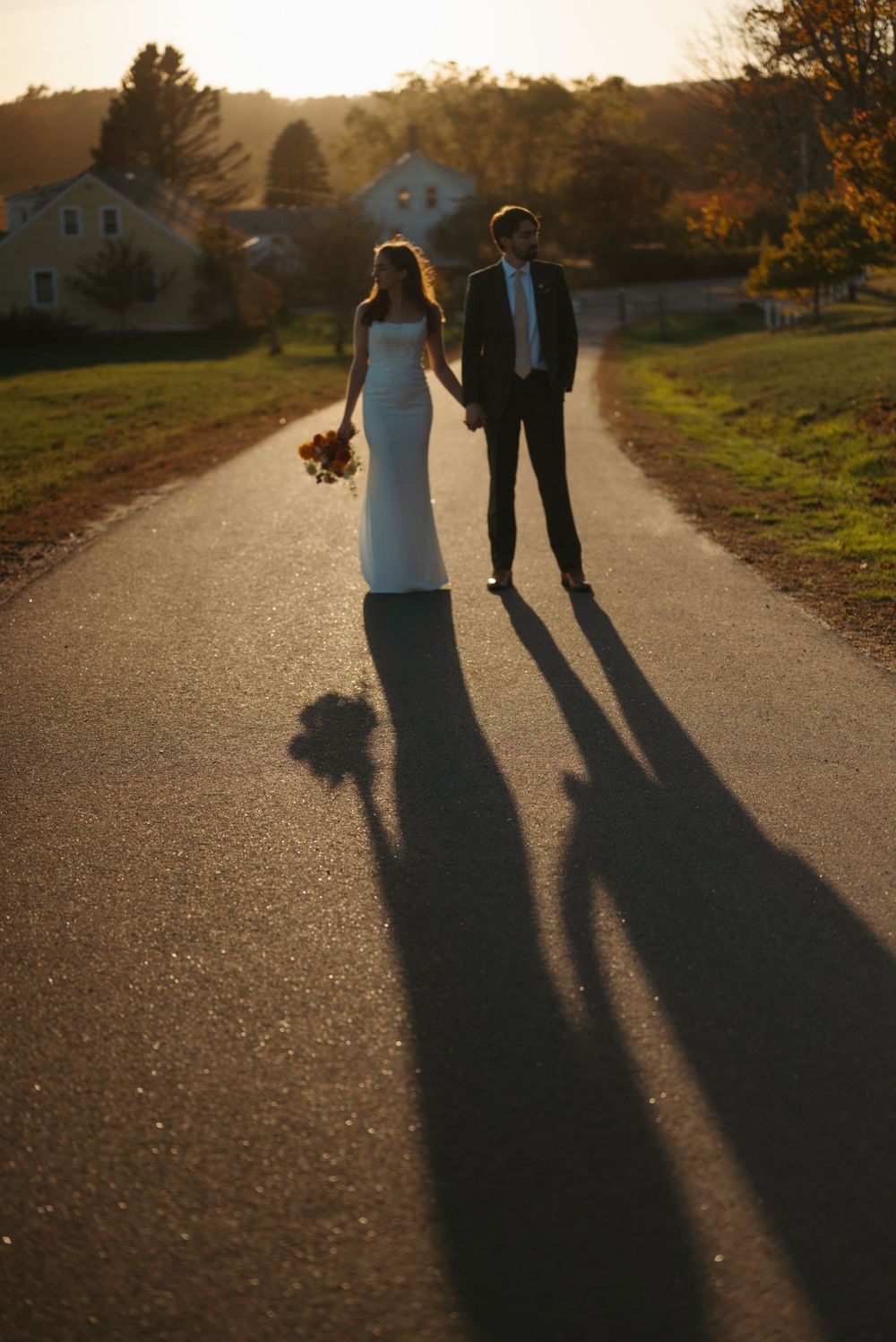 Long shadows of a couple walking on a country path at sunset with autumn foliage in the background.