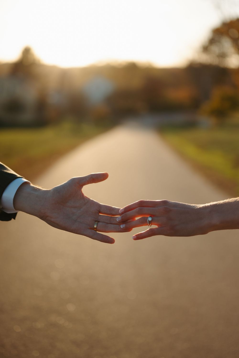 Two hands reaching towards each other at sunset on a rural path, creating a silhouette against the warm light.