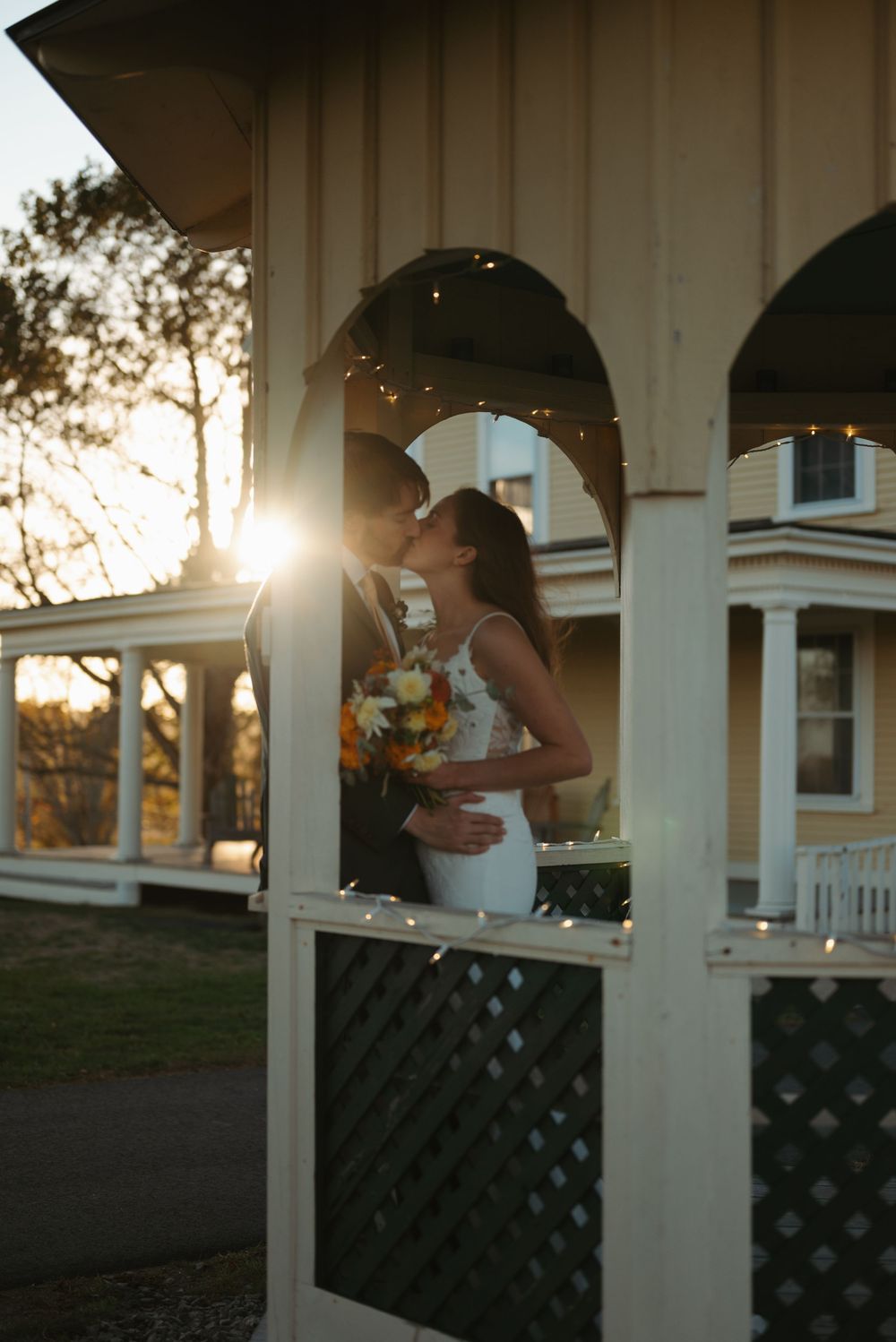A romantic sunset moment captured through white pillars on a porch with golden sunlight streaming through.