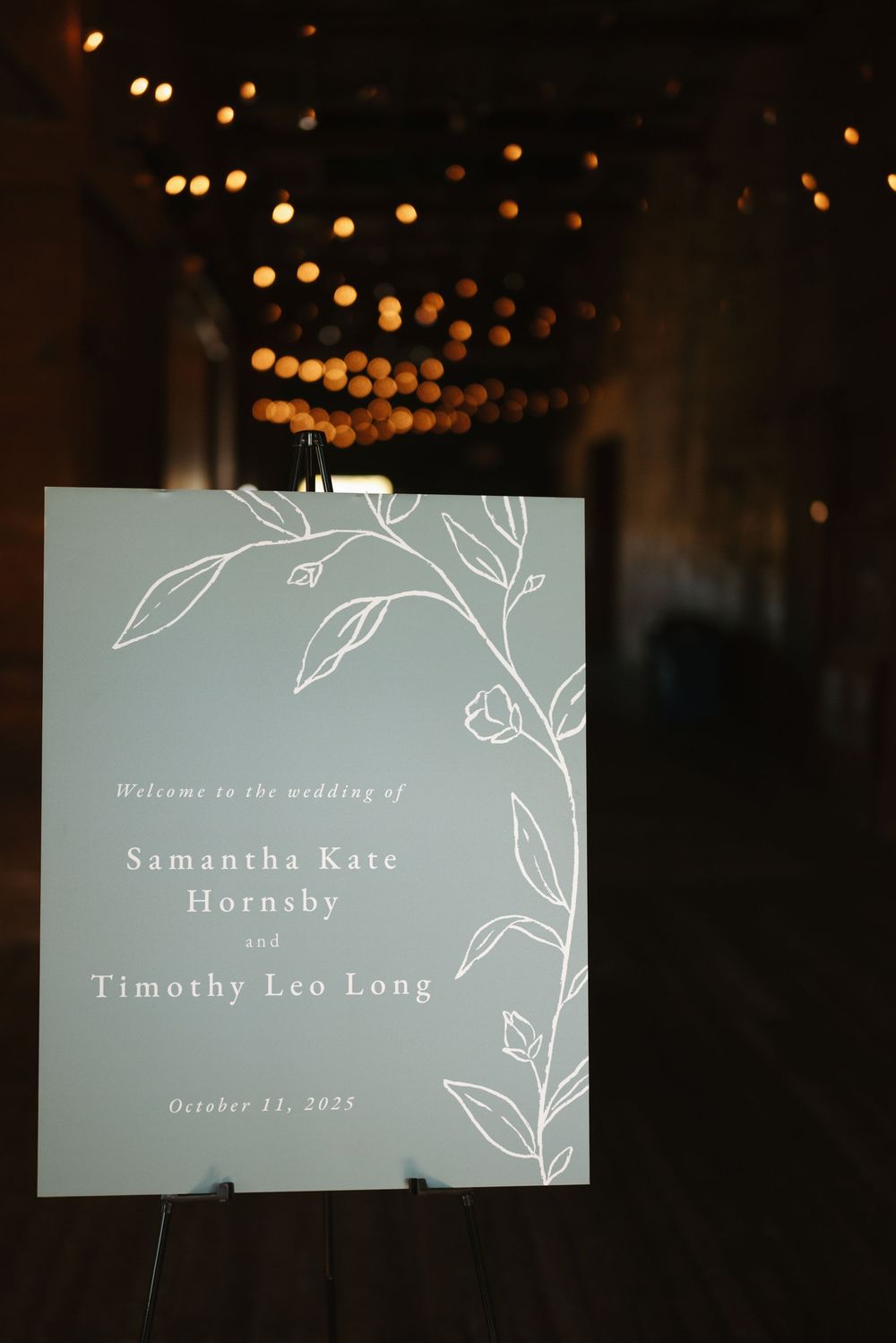 Wedding invitation text displayed on a light blue background with delicate floral line art and bokeh lights in the background.