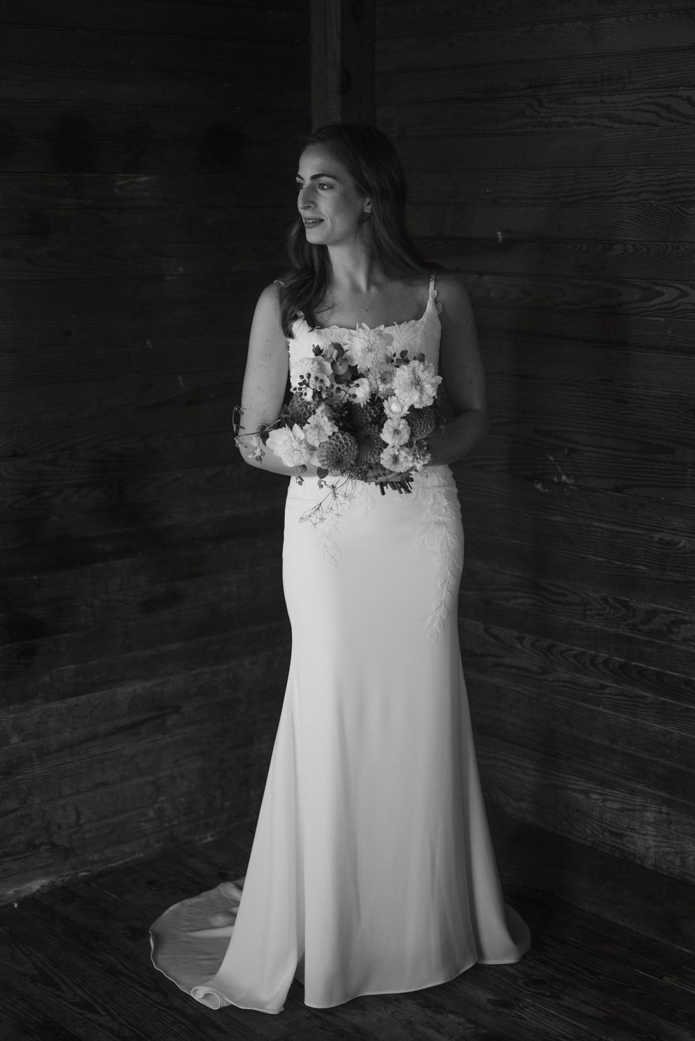 A white wedding dress with delicate floral details along the neckline photographed against a dark wooden backdrop.