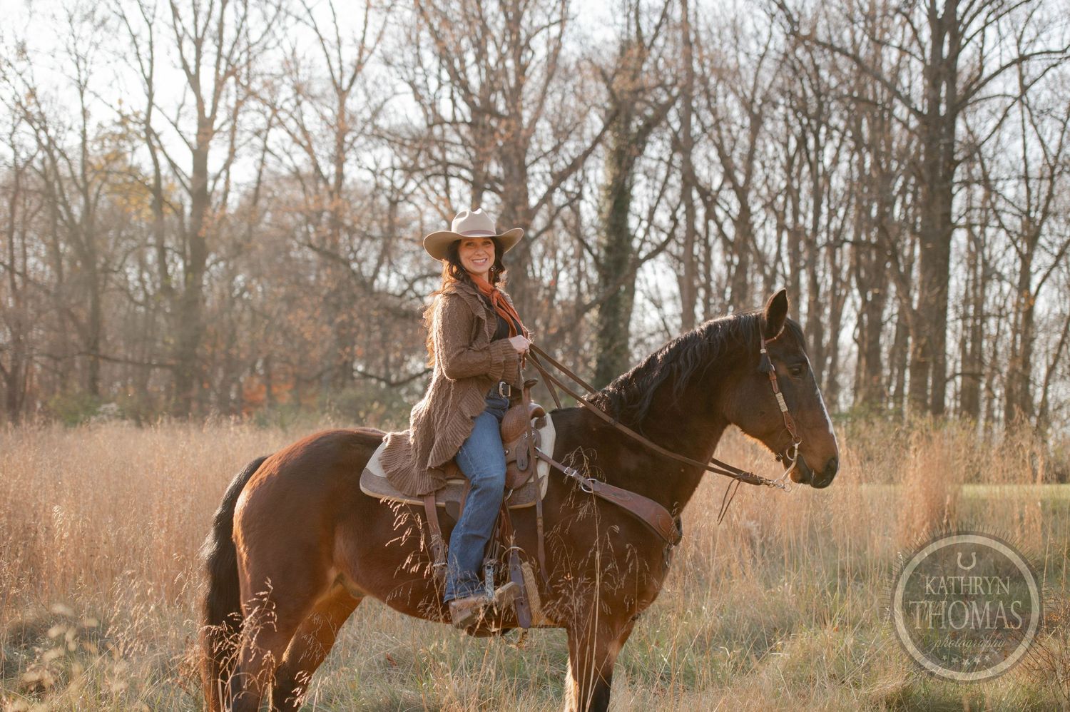 Horseback rider in western attire navigates through a sunlit field of tall autumn grass.