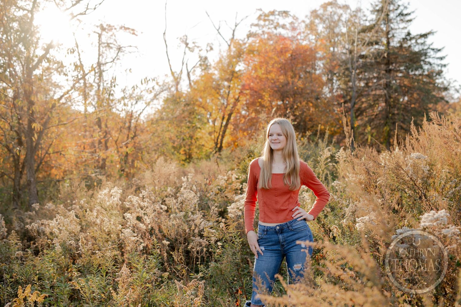 Casual outdoor portrait with orange top against autumn foliage and golden light.