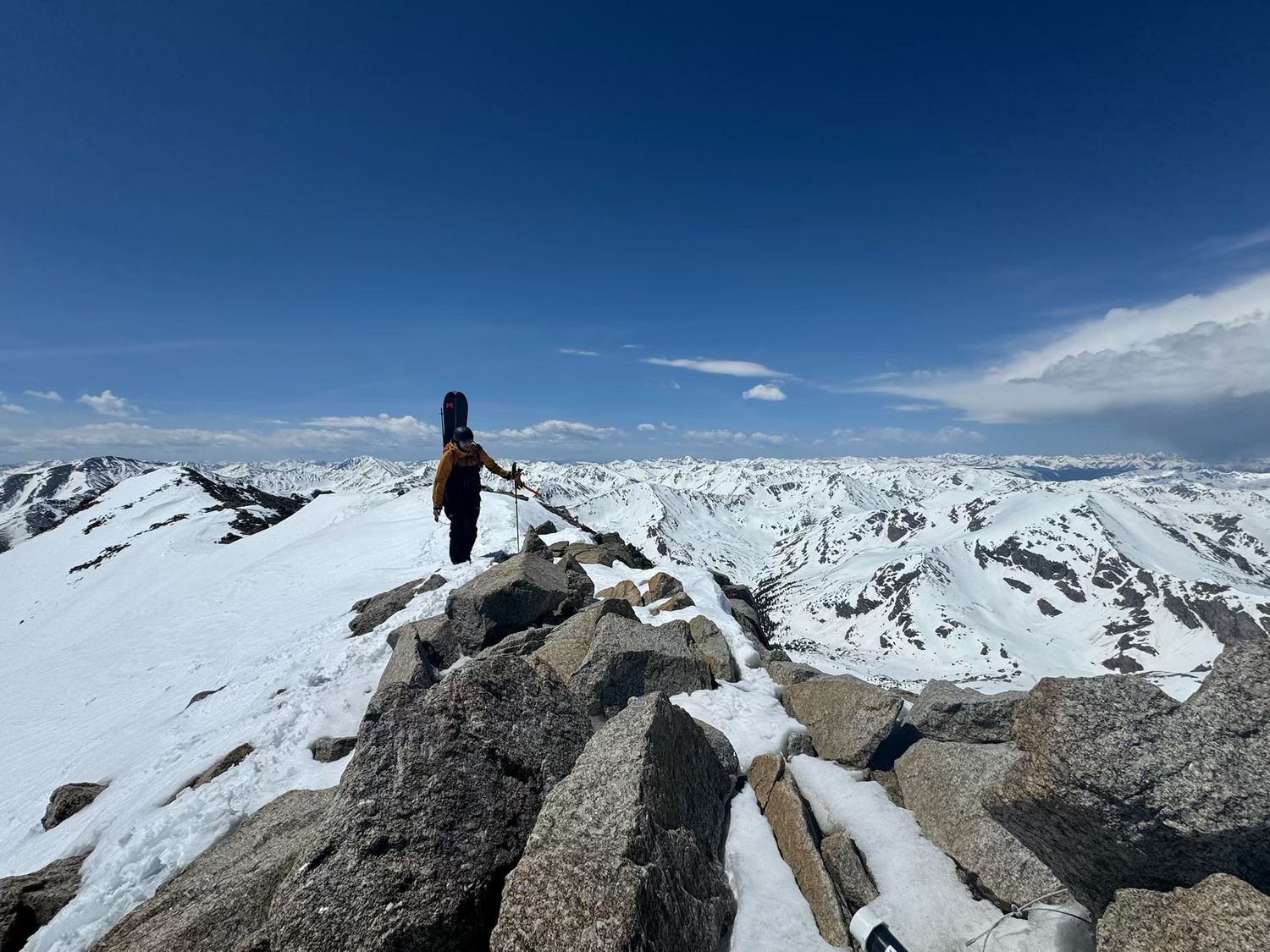 Snow-covered mountain peaks stretch across horizon under blue sky in panoramic winter landscape.
