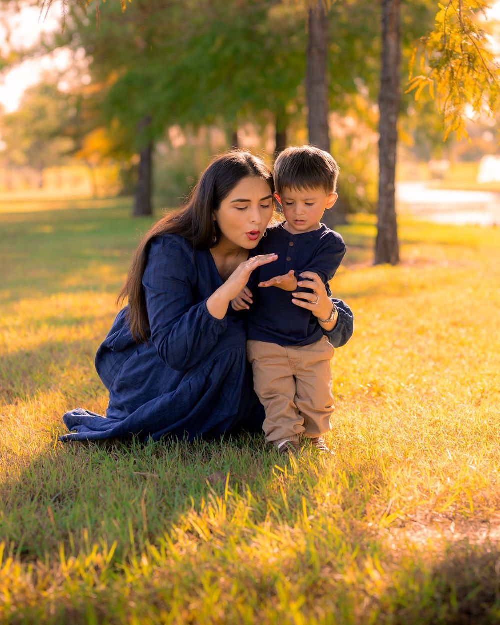 A parent and child share a tender moment on golden grass during sunset in a park setting. In Houston, TX